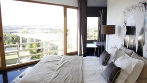 A large bed with multiple pillows, a view of the outdoors through a sliding door, and a painting on the wall. - Quinta do Molinu (Lourinha)
