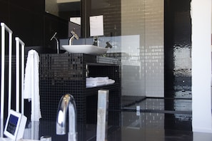 A modern bathroom with a black tiled vanity, a white sink, and a glass shower enclosure. - Quinta do Molinu (Lourinha)