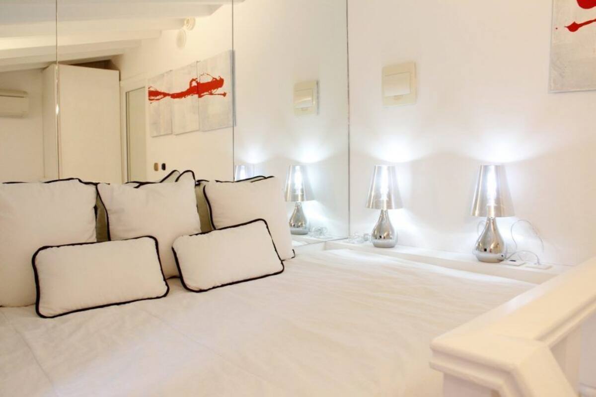 A hotel room with a large bed, white bedding, and multiple bedside lamps.