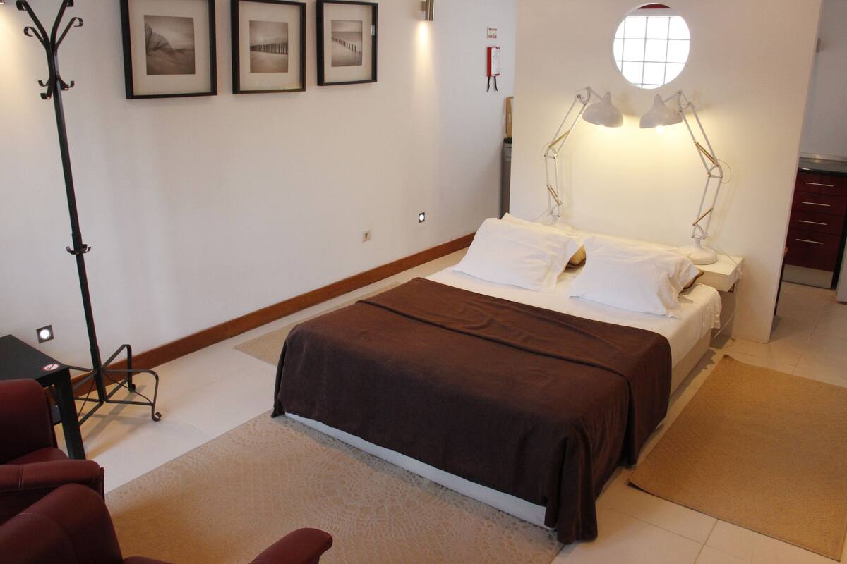 A hotel room with a bed, bedside table, lamp, and a chair.