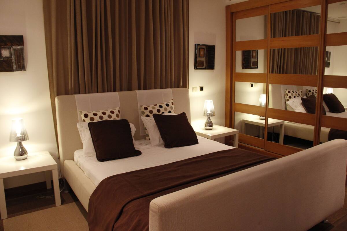 A hotel room with a bed, nightstands, a mirror, and a curtain.