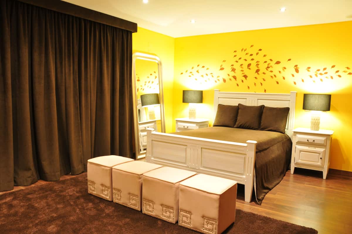 A bedroom with a bed, bedside tables, a mirror, and a wall with a leaf pattern.