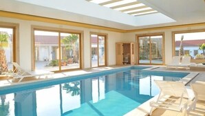 A modern indoor swimming pool with clear glass walls, large windows, and sunlit interior. - Quinta do Molinu (Lourinha)