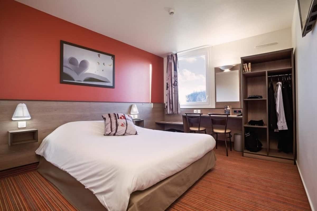 A hotel room with a bed, desk, chair, wardrobe, and a window with a view.