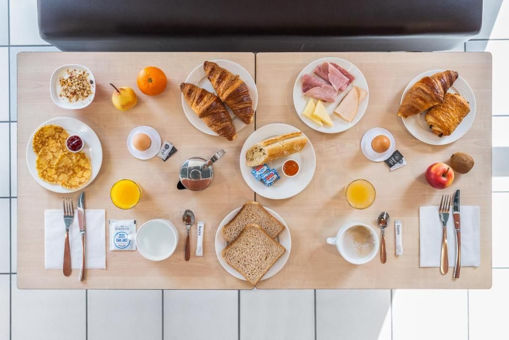 A breakfast table with croissants, ham, cheese, eggs, toast, fruit, and beverages.