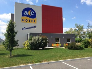 A hotel with a prominent sign, a small attached building, and outdoor seating. - Ace Hôtel Roanne-Mably (Mably)