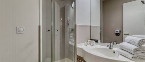 Een moderne badkamer met een douchecabine van glas, een wastafel met toiletartikelen en een spiegel.
