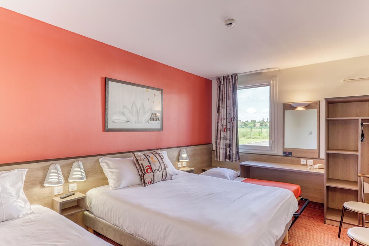 A hotel room with two beds, a desk, a chair, a wardrobe, a window with curtains, and a painting on the wall.