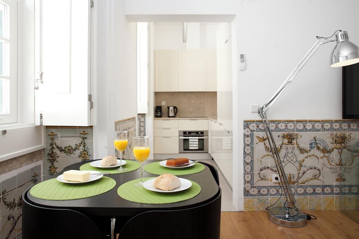 A dining area with a table set for two, a coffee maker, and a lamp.
