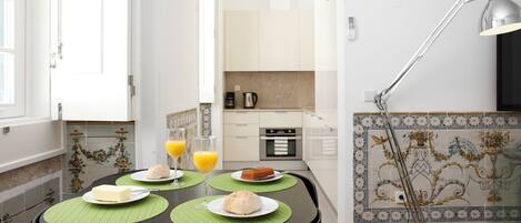 A dining area with a table set for two, a coffee maker, and a lamp.