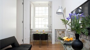 Un soggiorno moderno con un divano, un tavolo da pranzo con sedie, una finestra con persiane, una lampada e un vaso con fiori.