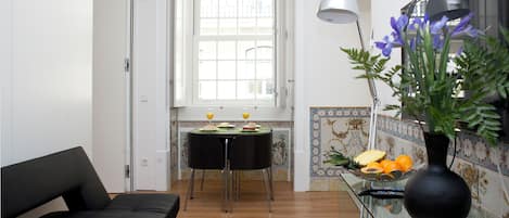Un salón moderno con sofá, una mesa de comedor con sillas, una ventana con persianas, una lámpara y un jarrón con flores.