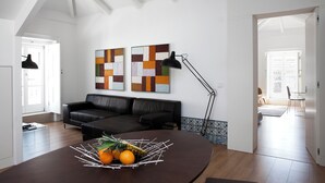Un soggiorno moderno con un divano in pelle nera, un tavolo da pranzo rotondo con della frutta, due quadri astratti e una lampada da terra nera.