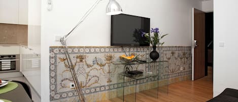 Una sala de estar moderna con televisor, una mesa de centro de vidrio, una lámpara de pie y un rebozado de azulejos decorativos.