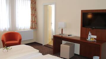 Ein Hotelzimmer mit einem Bett, einem Schreibtisch mit Fernseher, einem Sessel, einer Lampe und einer Heizung.
