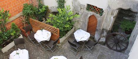 Un espace extérieur aménagé en terrasse, avec des tables et des chaises, un mur de briques et un mur de pierres agrémenté d’une porte en bois.