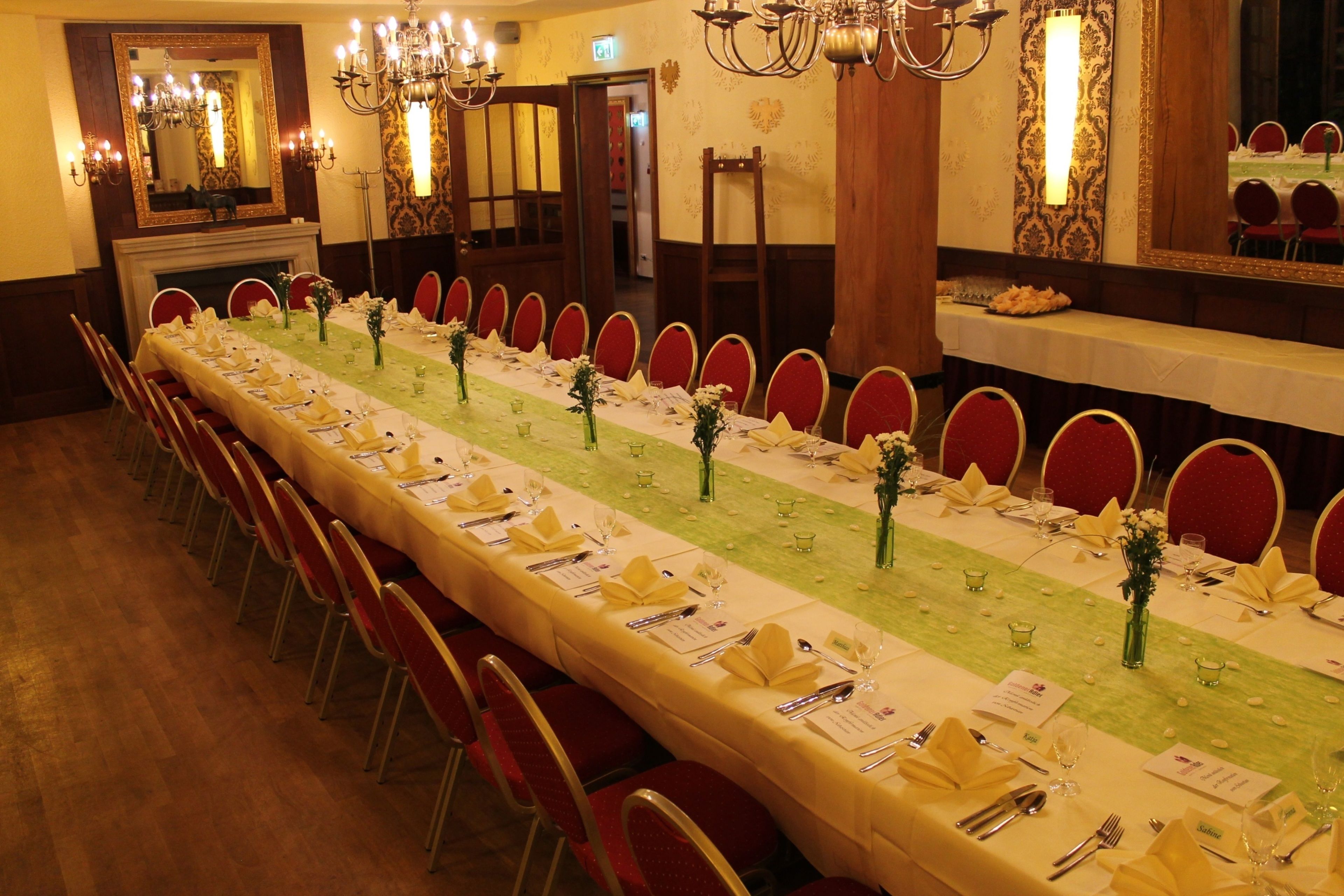 A long dining table set for a formal event with red chairs, a green table runner, and floral centerpieces.