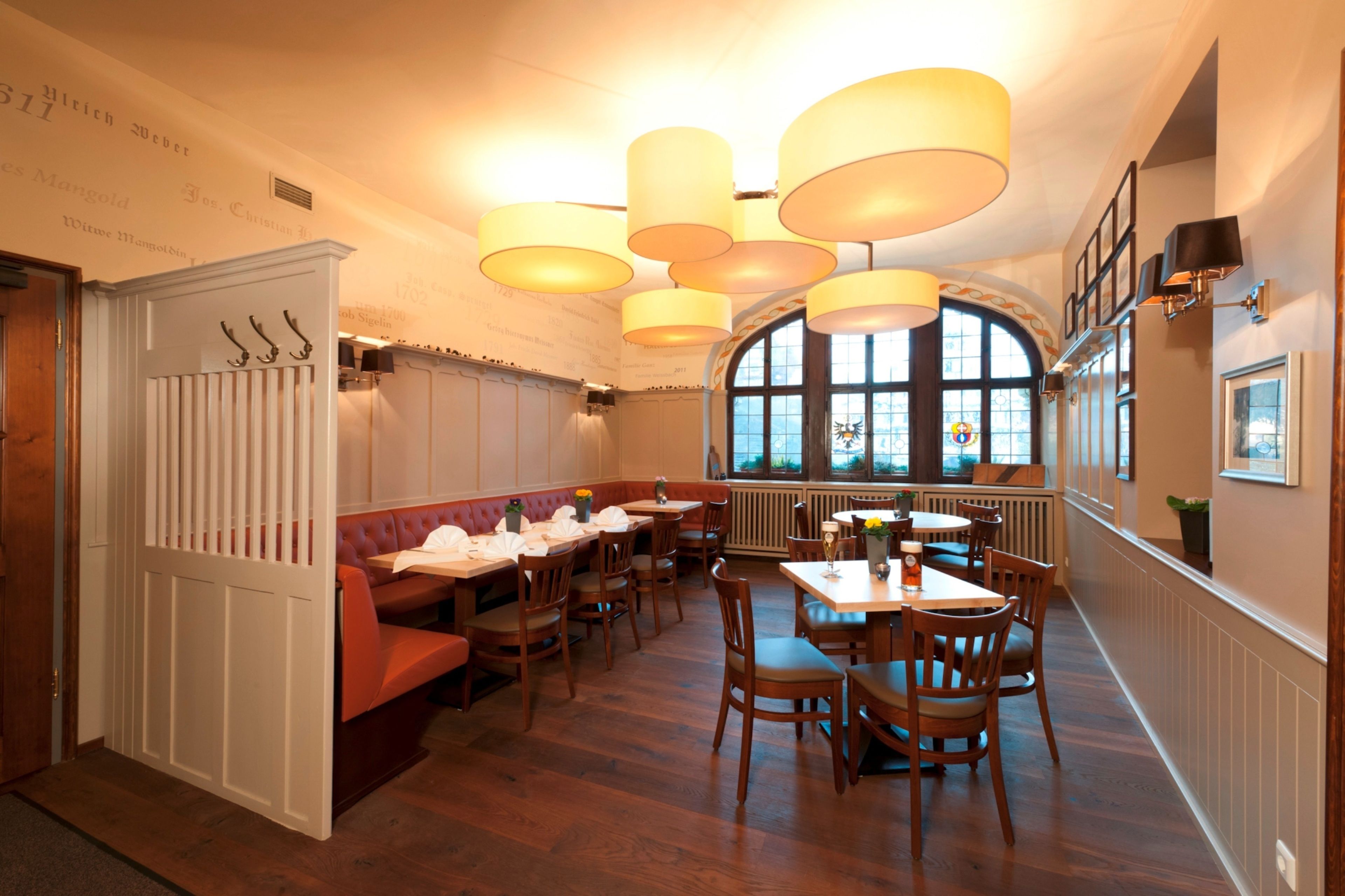 A restaurant interior with wooden tables and chairs, a red booth seating area, and large windows with a view.
