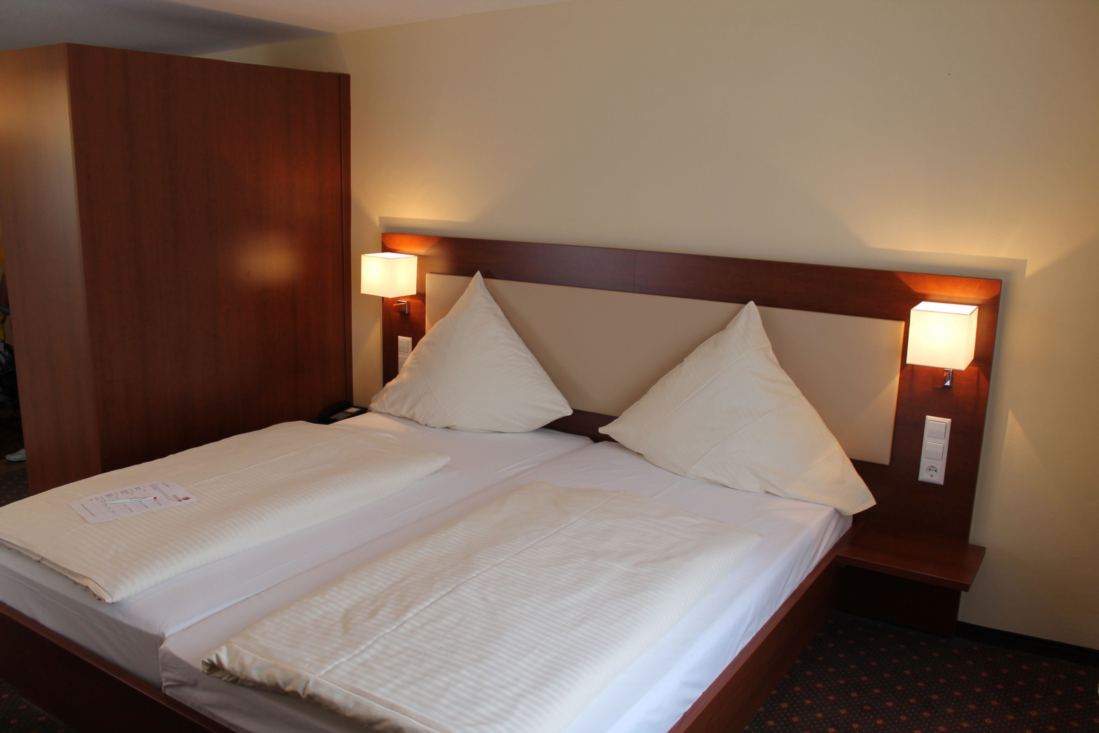 Een hotelkamer met een tweepersoonsbed, twee bedlampen, een houten hoofdeinde en een grote garderobe.