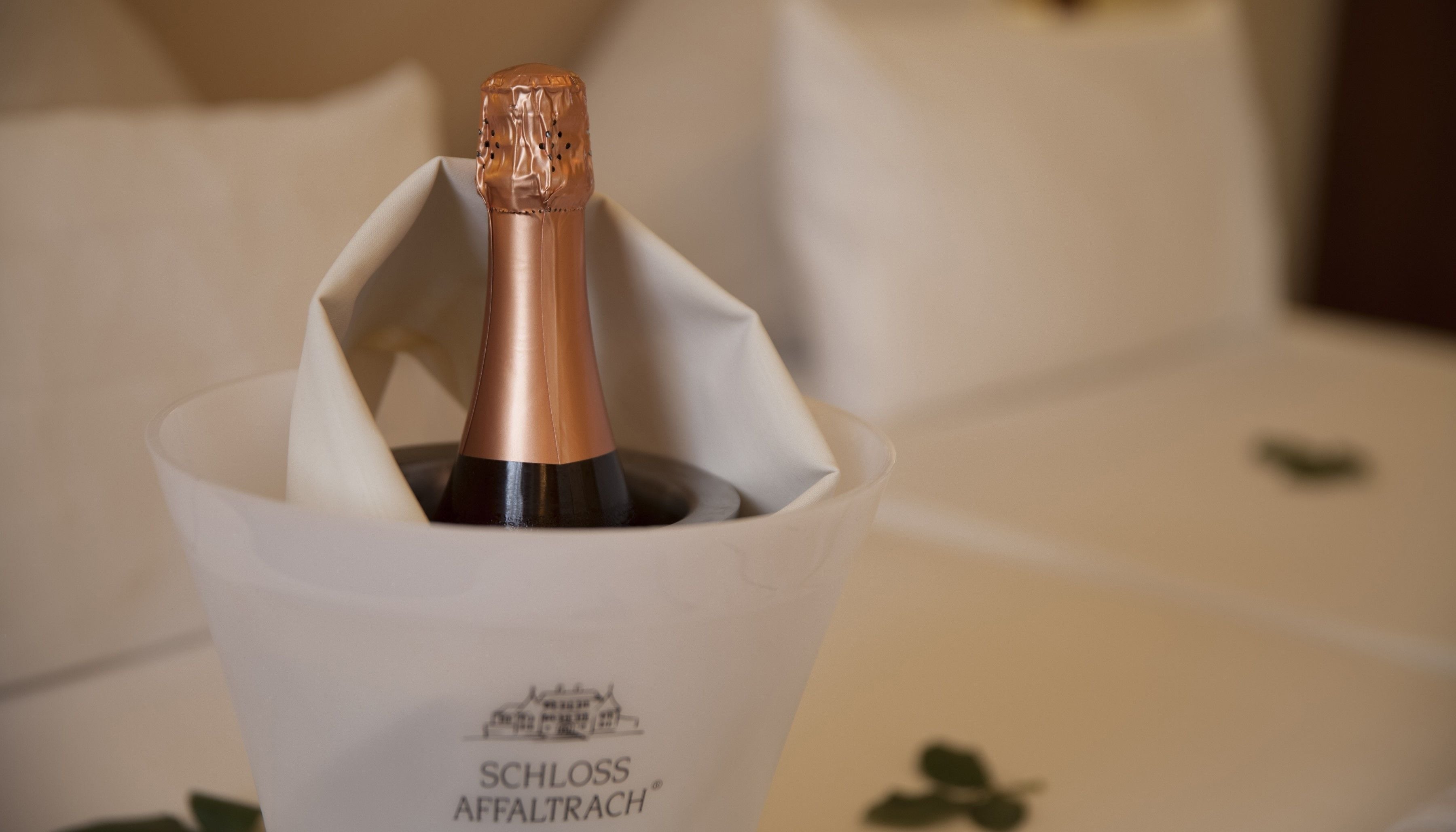 A bottle of SCHLOSS AFFALTRAUCH champagne in a white paper cup.