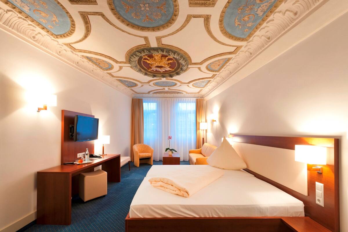 A hotel room with a large bed, a desk, a television, and a chair.
