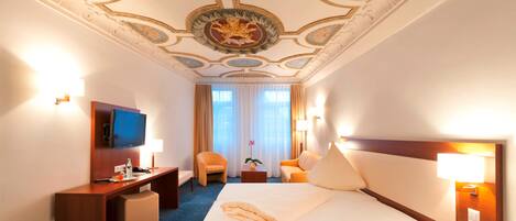 A hotel room with a large bed, a desk, a television, and a chair.