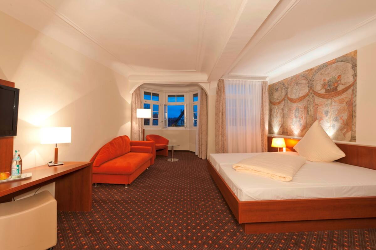 A hotel room with a bed, a desk, a chair, a sofa, and a window with curtains.