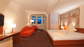 A hotel room with a bed, a desk, a chair, a sofa, and a window with curtains.