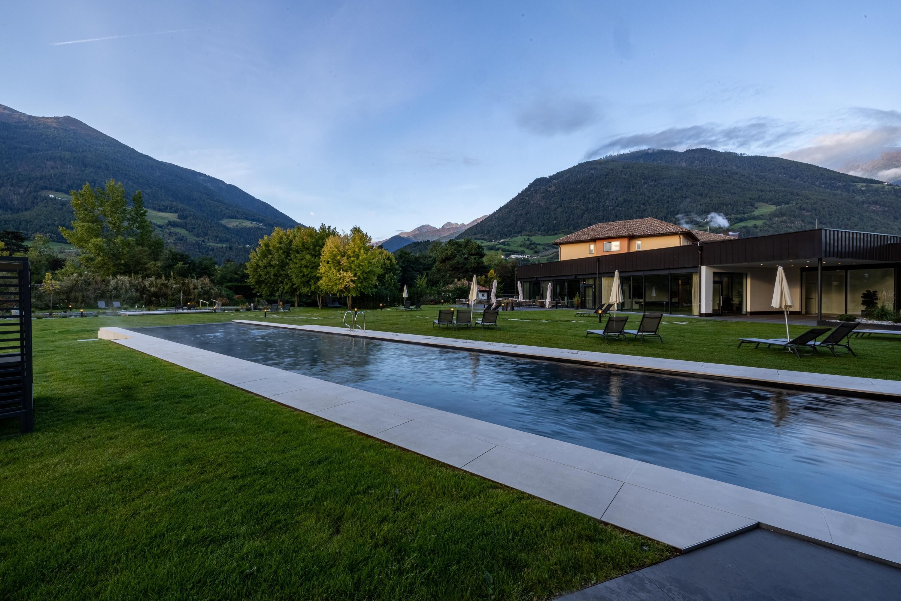 A swimming pool with lounge chairs, a building with a modern design, and a mountainous landscape in the background.