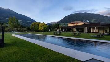 A swimming pool with lounge chairs, a building with a modern design, and a mountainous landscape in the background.