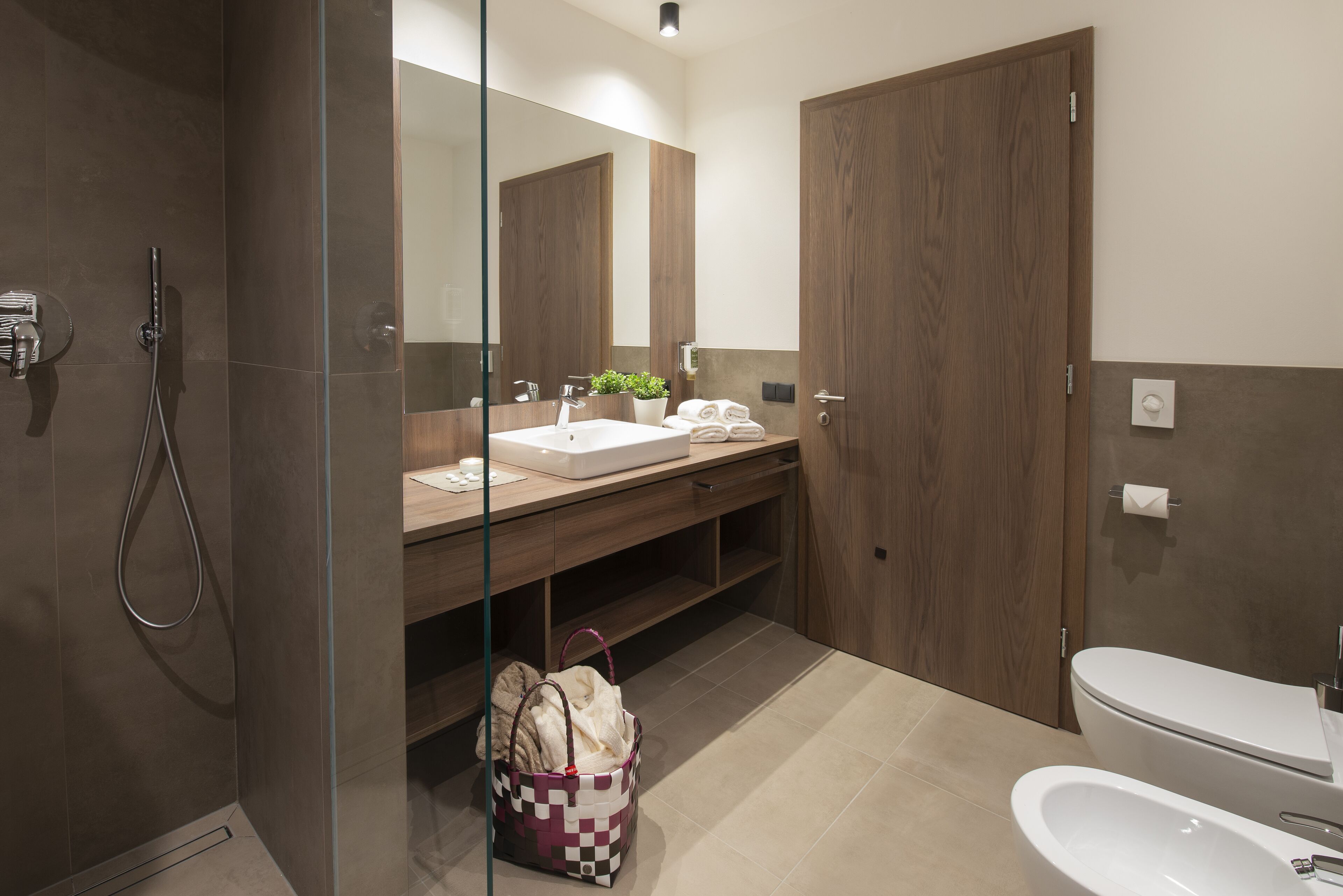 Un baño moderno con ducha envuelta en vidrio, tocador de madera con lavabo y un inodoro.