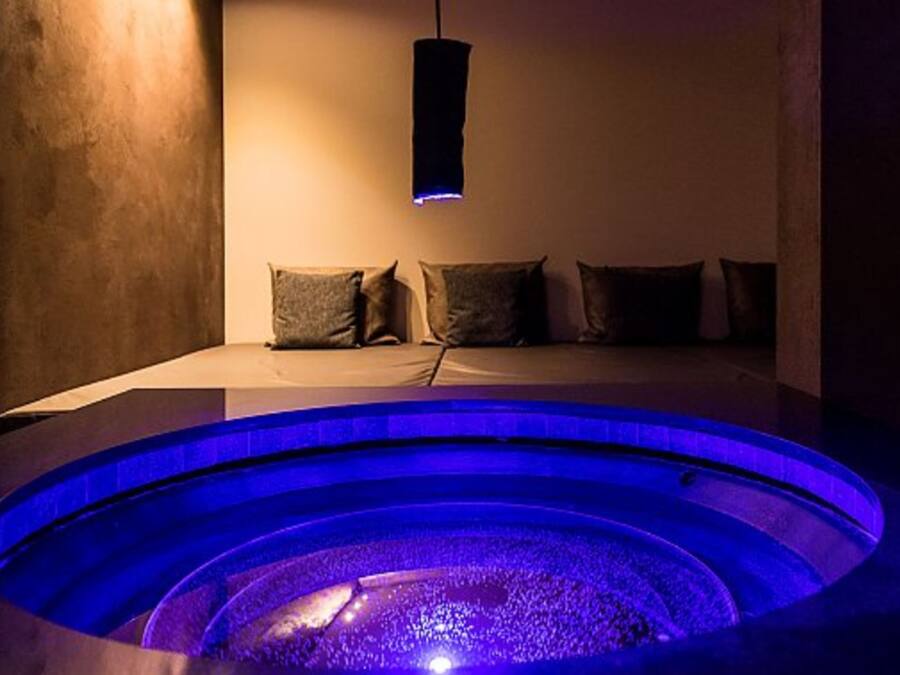 Una habitación con una bañera de hidromasaje circular, una cama con almohadas y un lámpara colgante.