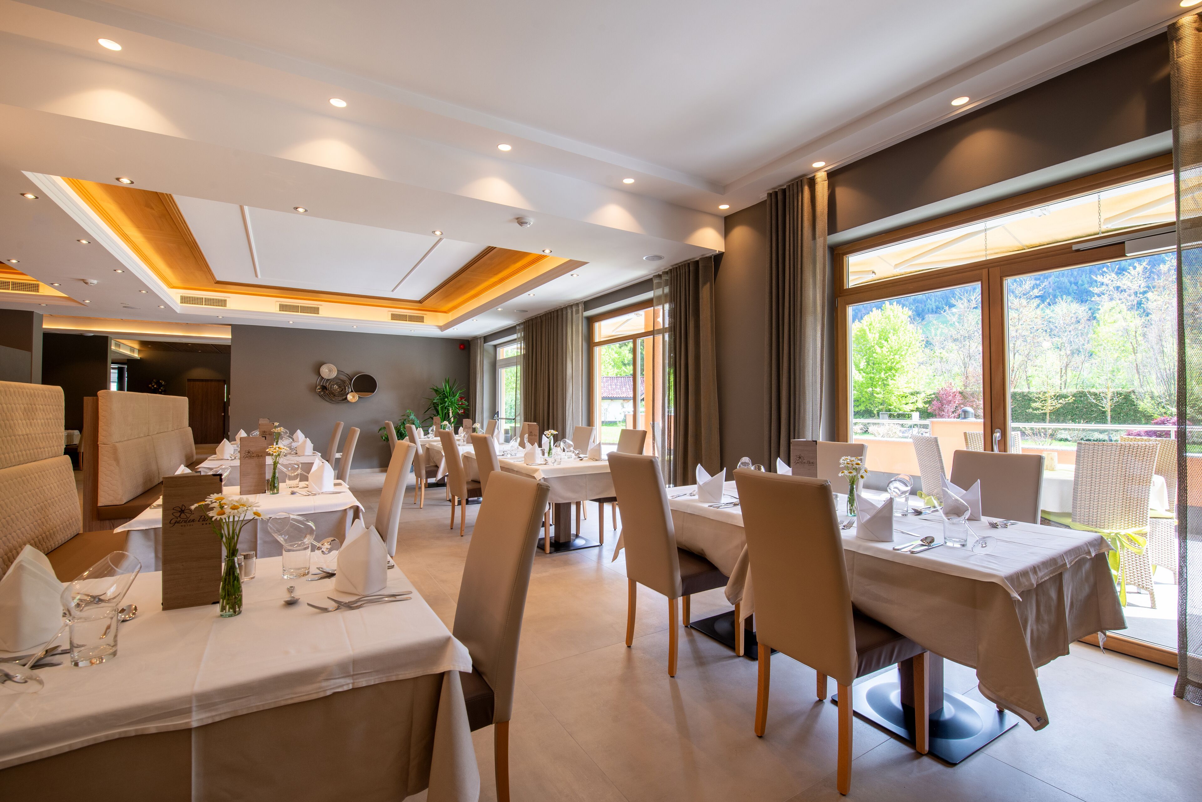 Un restaurante con varias mesas dispuestas para comer, amplias ventanas con vistas a zonas verdes y un diseño de techo moderno.