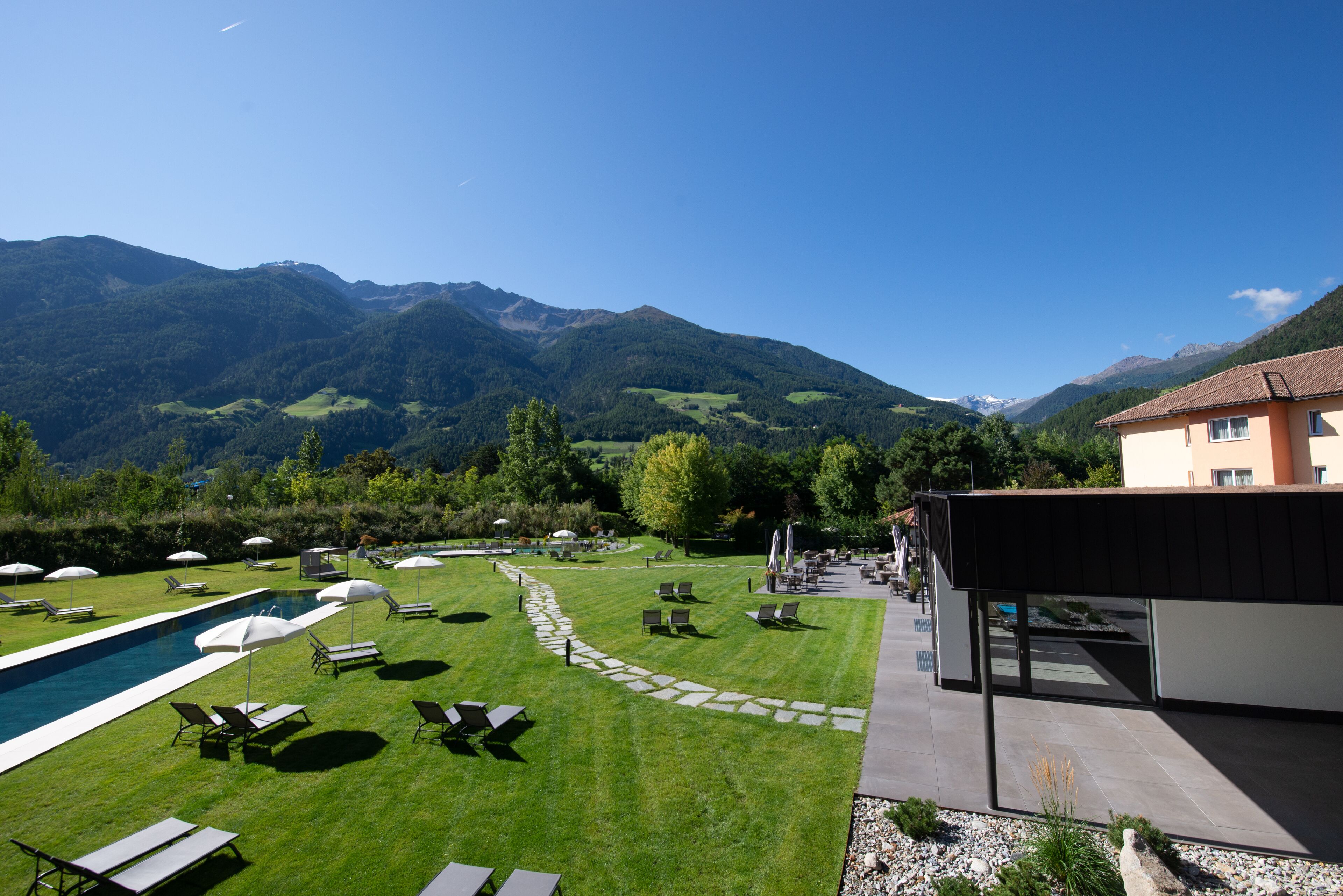 A poolside area with lounge chairs and umbrellas, a stone pathway, and a view of mountains.