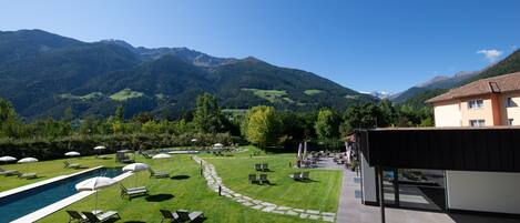 A poolside area with lounge chairs and umbrellas, a stone pathway, and a view of mountains.