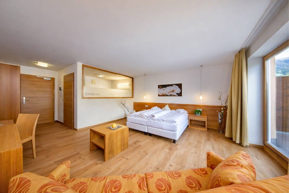 Une chambre d’hôtel avec un lit, un canapé, une petite table, un miroir et une fenêtre avec des rideaux.