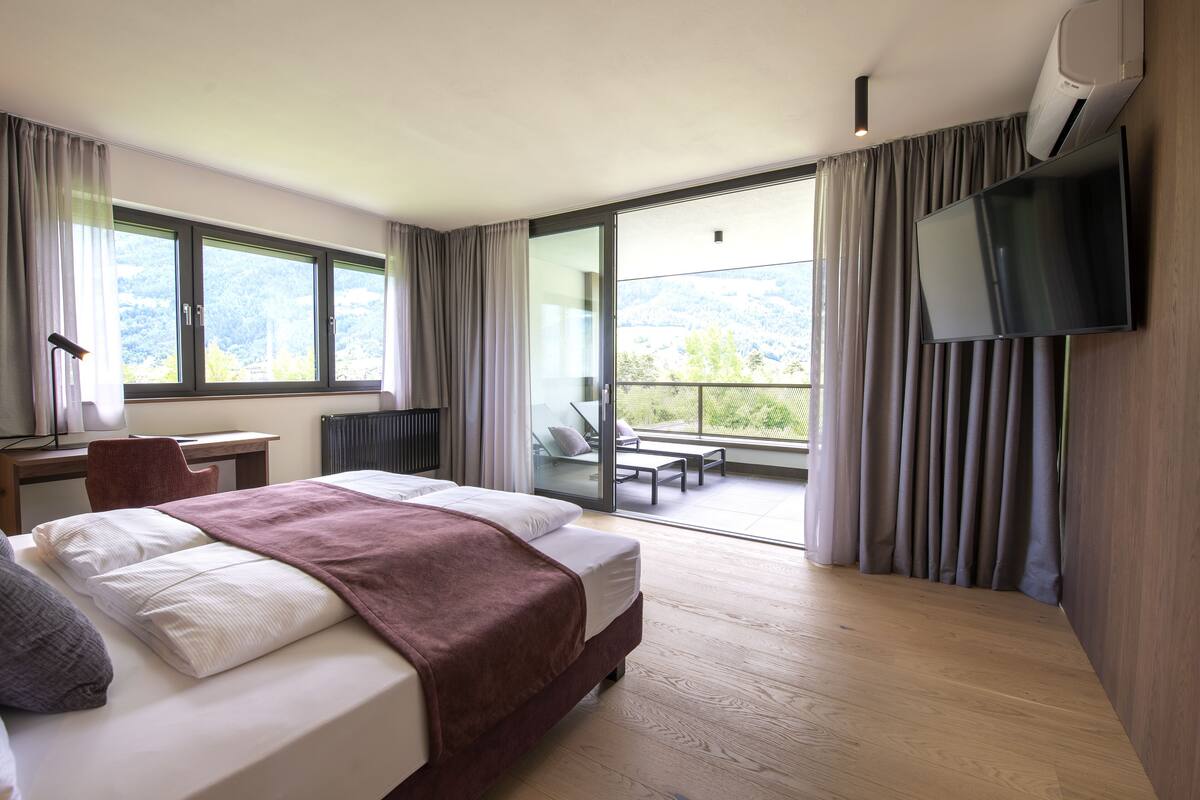 Une chambre d’hôtel moderne dotée d’un grand lit, d’un bureau et d’un balcon offrant une vue sur les montagnes.