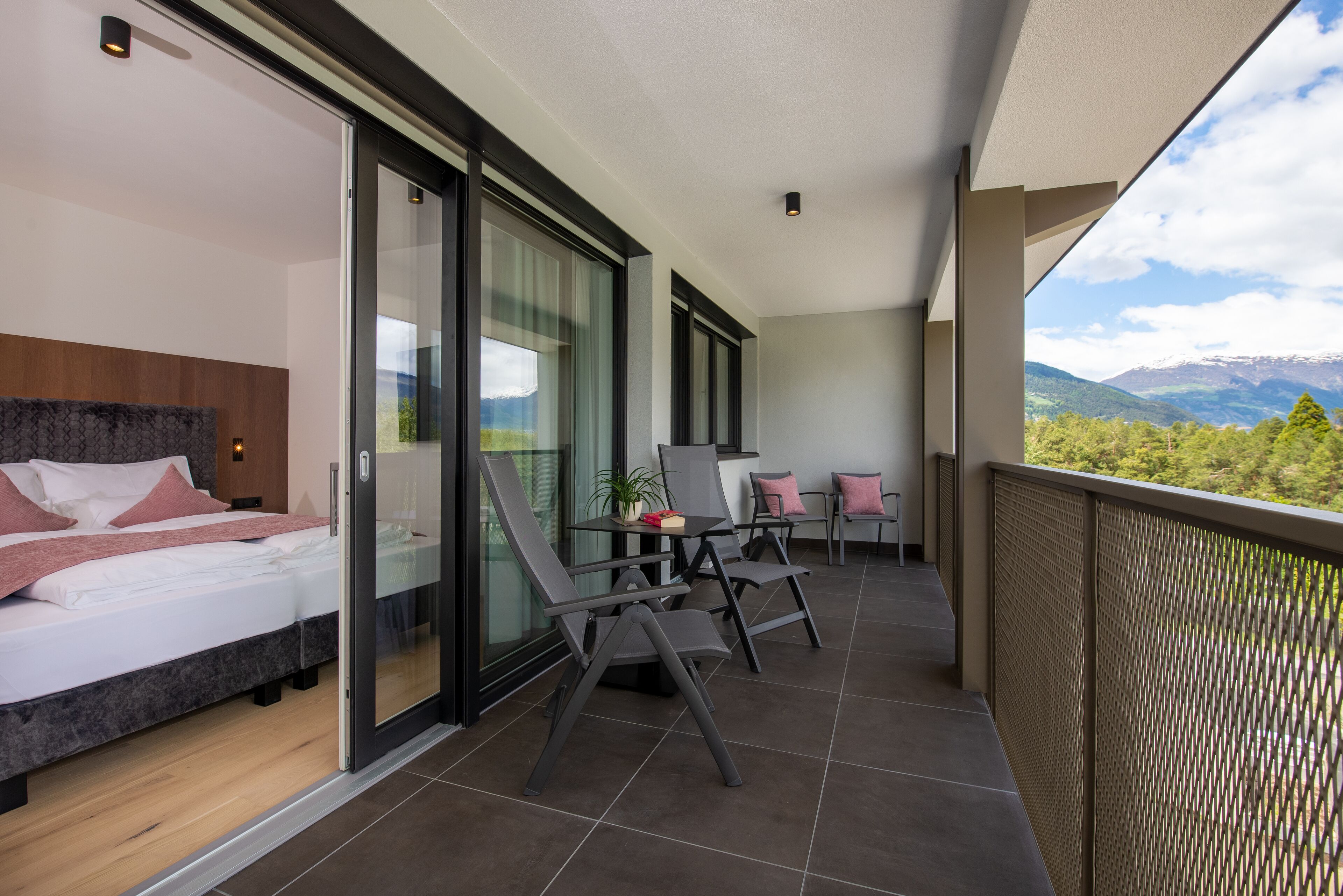 Una habitación de hotel moderna con balcón, cama, escritorio y vistas a las montañas.