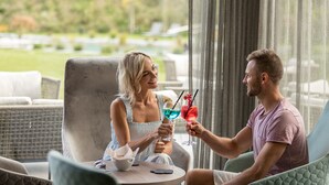 Una pareja sentada en una mesa con bebidas, con vista a un jardín.