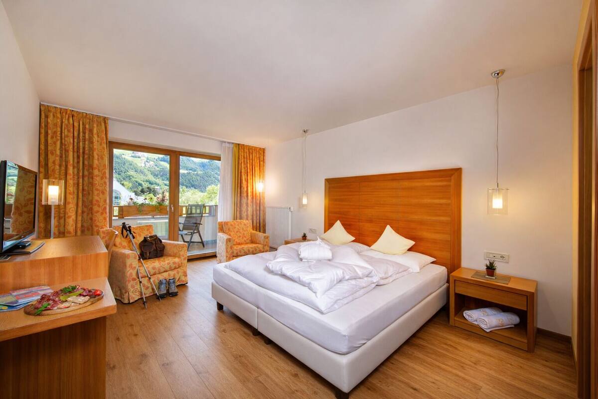 Une chambre d’hôtel avec un lit, un bureau avec une télévision, une chaise, une petite table avec de la nourriture, et une vue sur la verdure à l’extérieur.