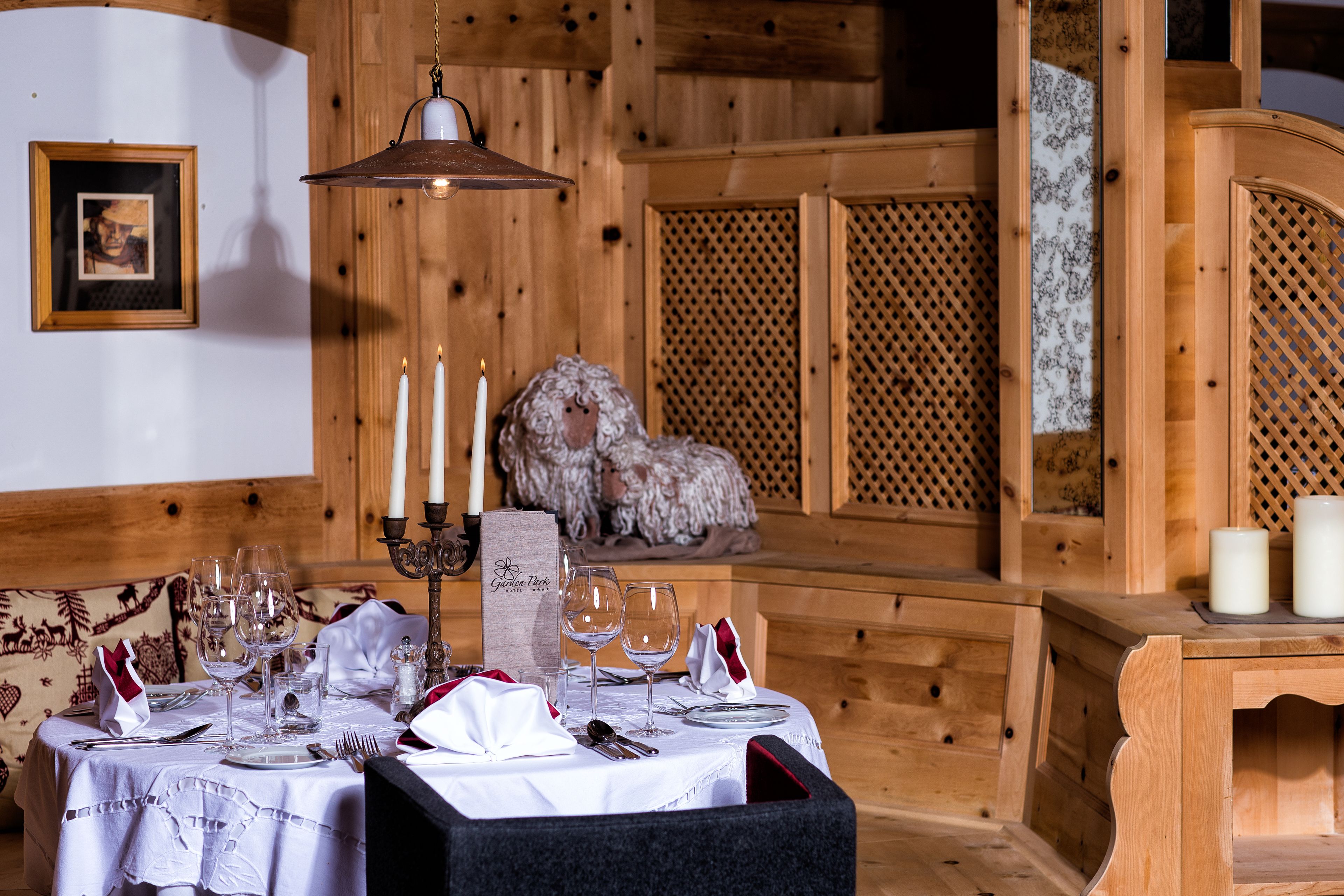 Interior de una cabaña de madera con una mesa de comedor dispuesta para cuatro personas, velas y un cuadro en la pared.