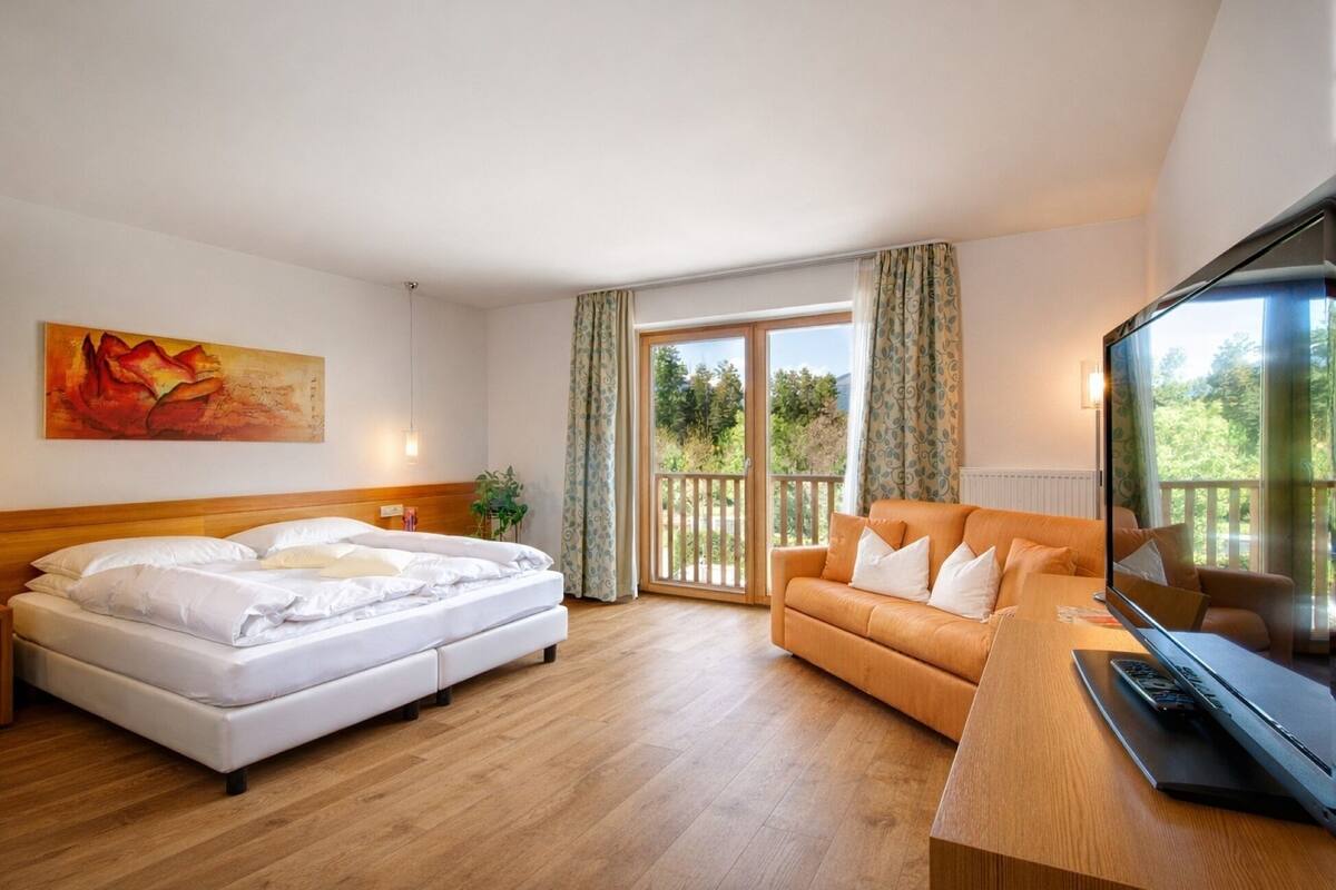 Une chambre d’hôtel avec un lit, un canapé, une télévision et un balcon avec des rideaux.