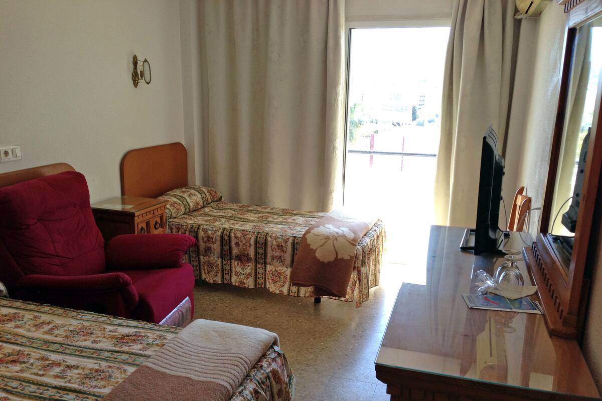 A hotel room with two beds, a wooden desk, a chair, and a window with curtains.