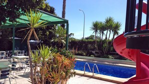 Un área de piscina con tobogán, palmeras y mobiliario de exterior.