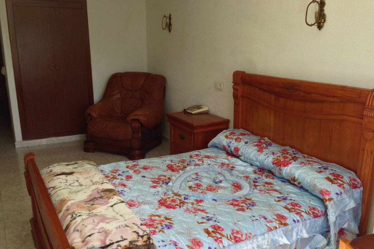 A bedroom with a wooden bed, a chair, a nightstand, and a door.