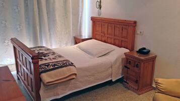 A bedroom with a wooden bed, a bedside table with a phone, a nightstand, and a small cabinet.