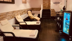 Un cuarto de spa con dos sillones reclinables, una pared de piedra, una pequeña escalera y un refrigerador para bebidas.