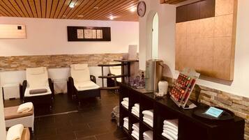 Un cuarto de spa con dos sillas de masaje, una recepción con toallas, un reloj y una pared de piedra.