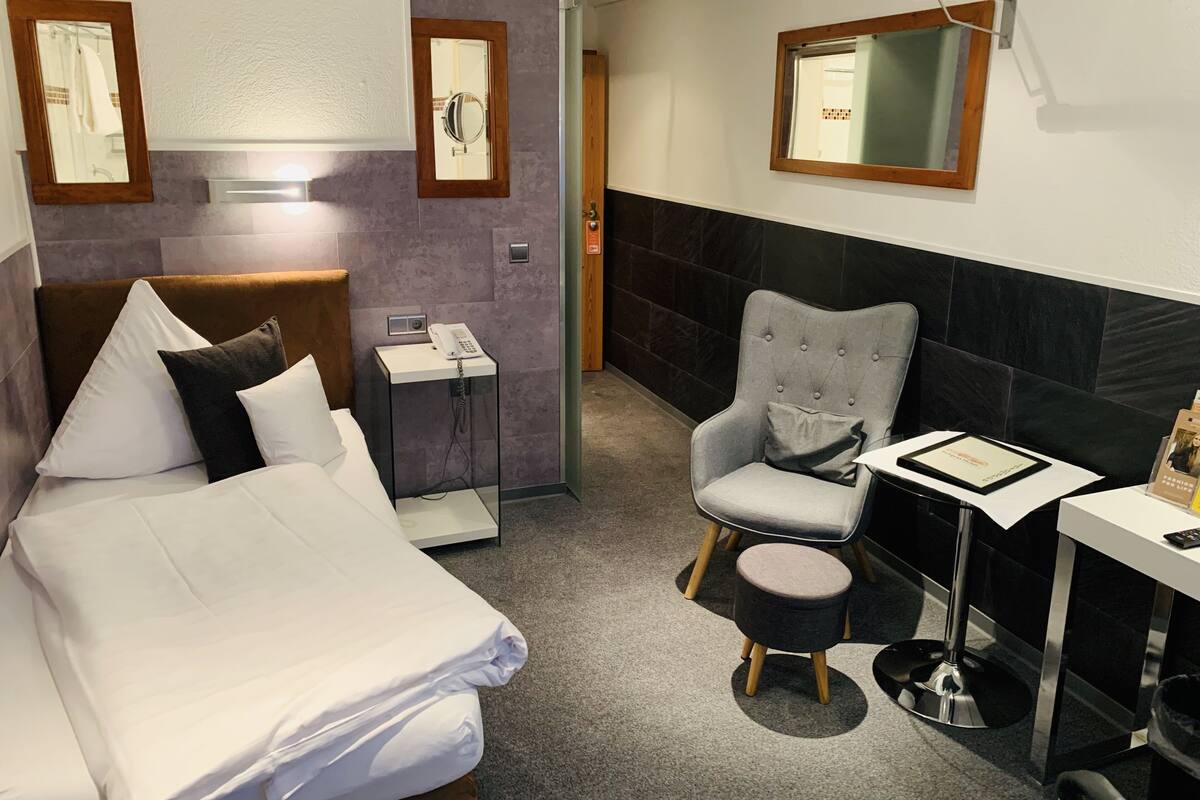 A hotel room with a bed, a chair, a small table, and a mirror.