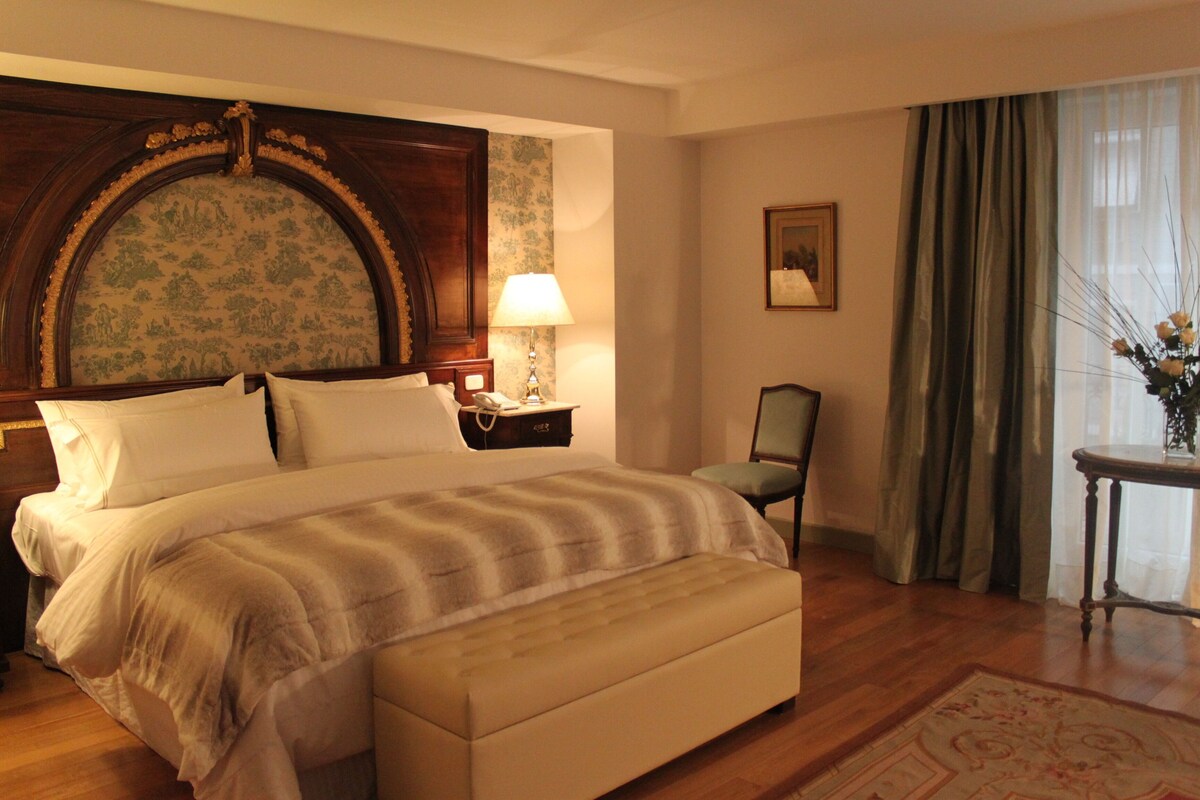 A hotel room with a large bed, a nightstand, a chair, a desk, and a window with curtains.